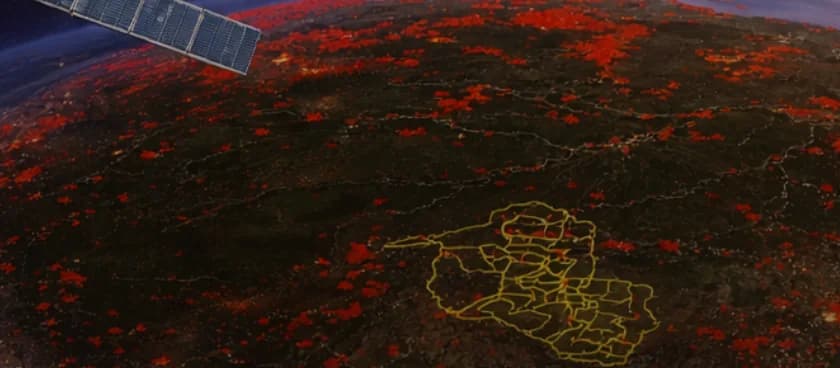 Vista orbital da Amazônia à noite com focos de calor em vermelho, Rondônia contornada em amarelo com suas divisas municipais, e o painel solar de um satélite atravessando o canto superior esquerdo